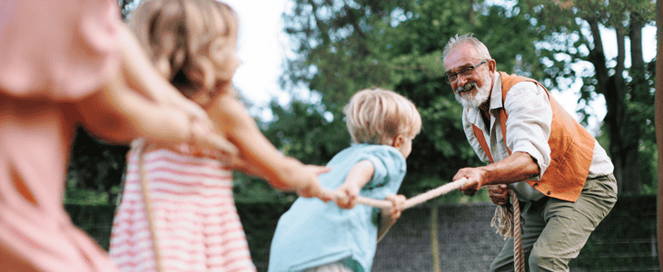 A grandfather gleefully plays tug of war with grandkids